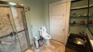Een badkamer met douche, toilet, wastafel en planken met toiletartikelen.