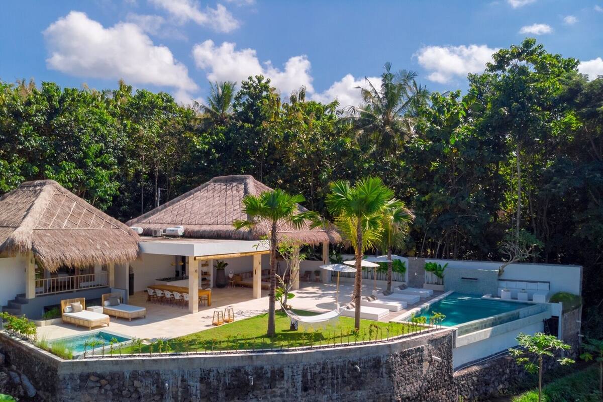 Ein Resort mit Pool, strohgedeckten Häusern und üppiger Vegetation.
