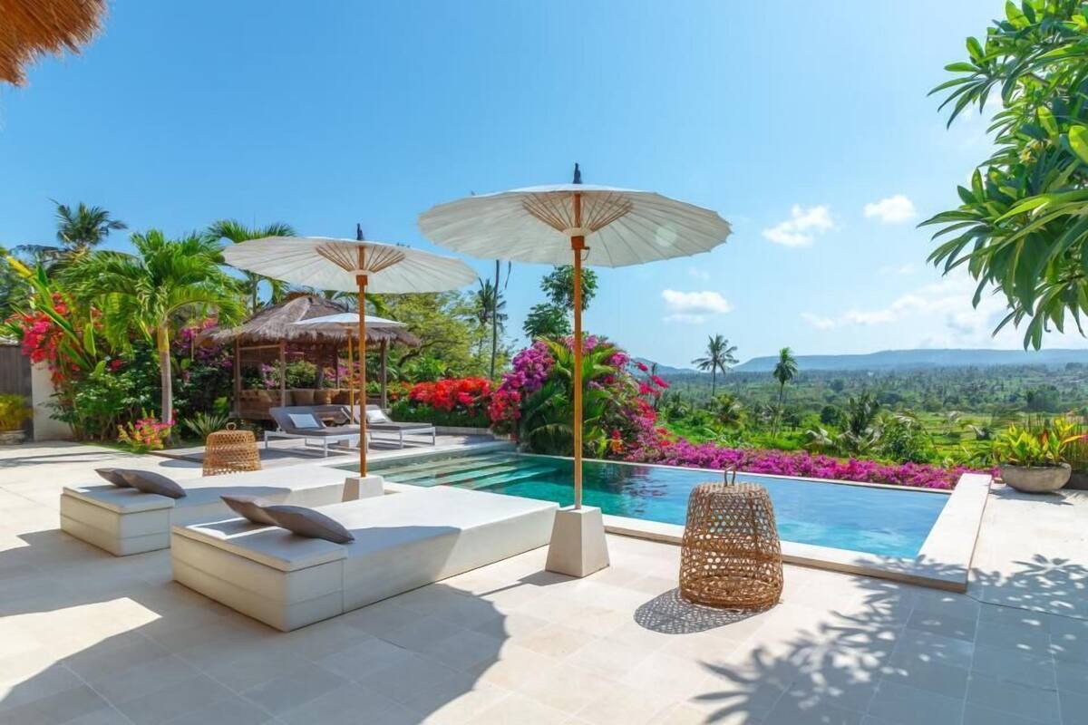 Ein Poolbereich mit Liegestühlen, Sonnenschirmen und Blick auf eine üppige Landschaft.