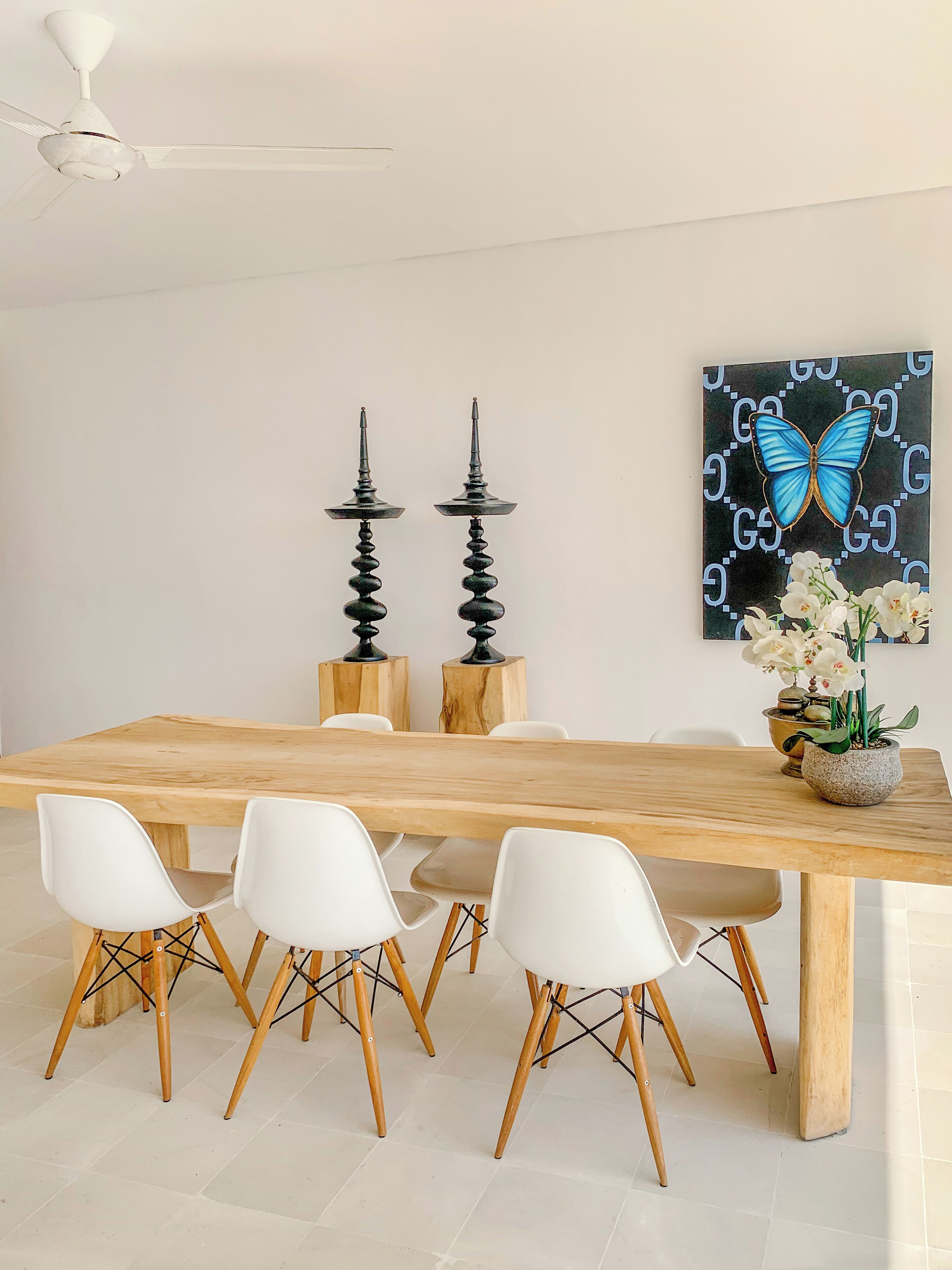 Un comedor con una mesa de madera, sillas blancas y un ventilador de techo.