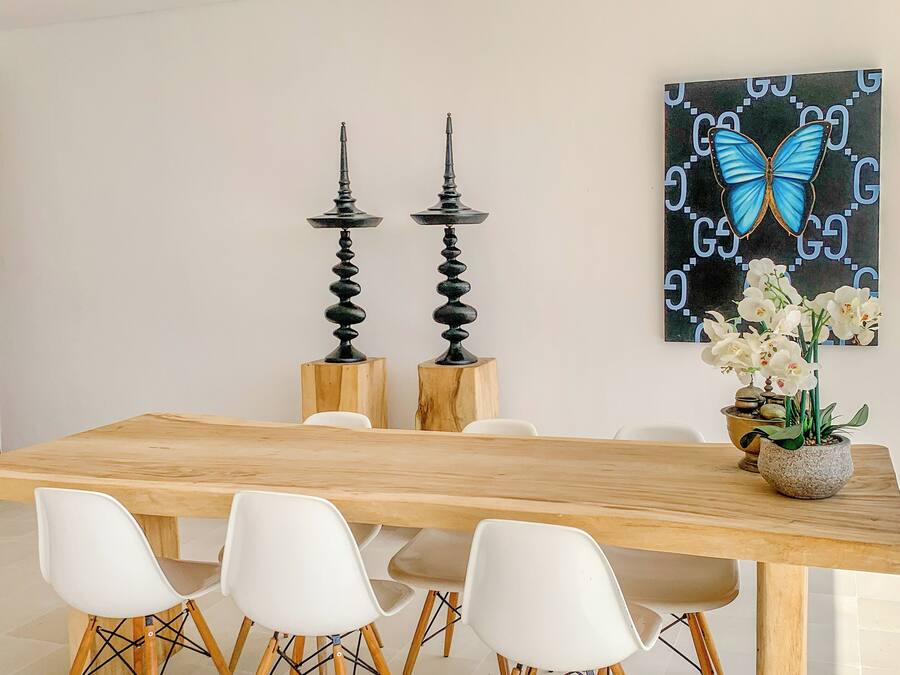 Un comedor con una mesa de madera, sillas blancas y un ventilador de techo.