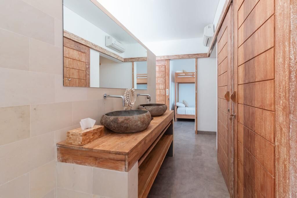 Un baño moderno con un tocador de madera, dos lavamanos de piedra grandes y un espejo.