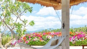 A hammock under a thatched roof, surrounded by wooden tables and vibrant flowers. - Balidroomvillas (Karangasem)