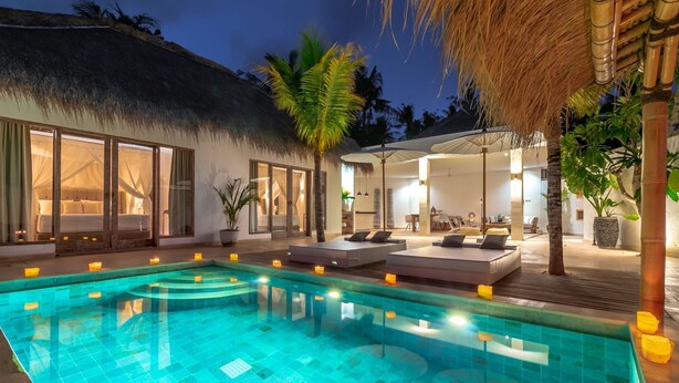A pool area with a thatched-roof structure, lounge seating, and a well-lit interior space. - Balidroomvillas (Karangasem)