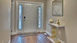 A hallway with a white door, a glass door with a decorative pattern, a console table with a gold base, and a framed mirror on the wall. - Walk to Grand Bend Main Beach | Sleeps 8 | Family Friendly | Heart of Grand Bend (Grand Bend)