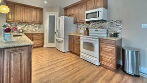 A kitchen with wooden cabinets, a refrigerator, a microwave, an oven, and a stainless steel trash can. - Walk to Grand Bend Main Beach | Sleeps 8 | Family Friendly | Heart of Grand Bend (Grand Bend)