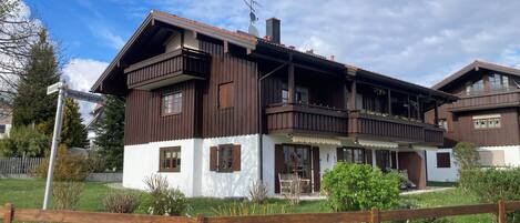 Un edificio de estilo chalé tradicional, con techo inclinado, balcones de madera y una entrada con banco.