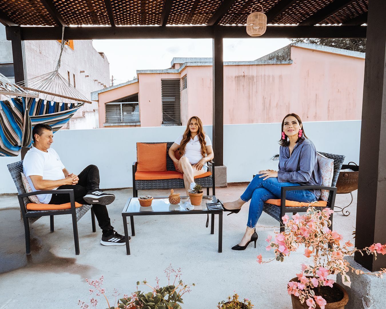 Un área de estar al aire libre con techo, una mesa, sillas y plantas en macetas.