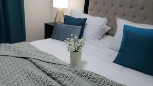 Een keurig opgemaakt bed met een gebreide deken, een potplant en een bedlampje.