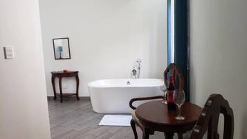A bathroom with a bathtub, a small table with a bottle and glass, and a chair.