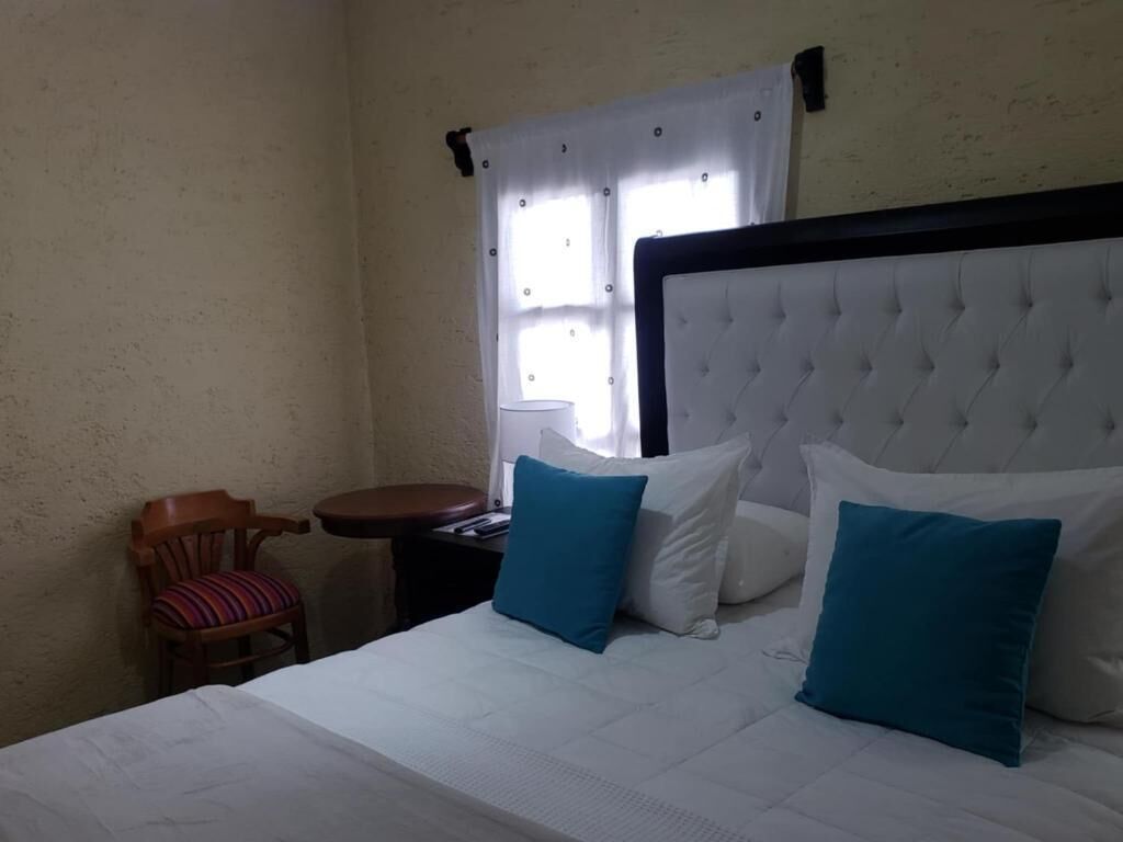 A hotel room with a bed, two pillows, a chair, a small table, and a window with curtains.