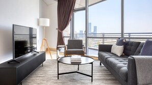 Una habitación de hotel moderna con un ventanal grande, un sofá, una mesa de centro, un televisor y una lámpara.