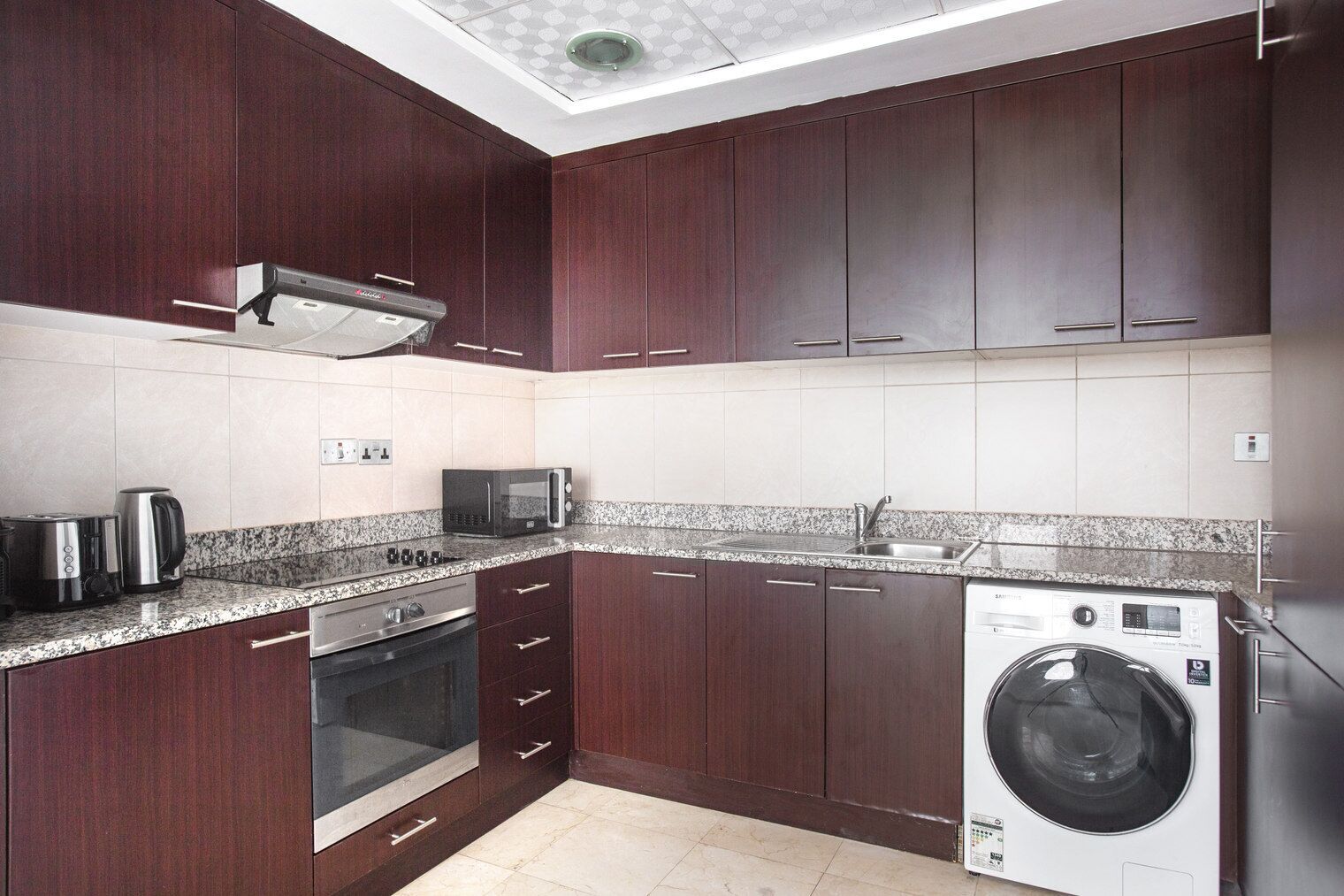 Una cocina moderna con armarios de madera oscura, un lavamanos de acero inoxidable, un microondas, un tostador y una lavadora.