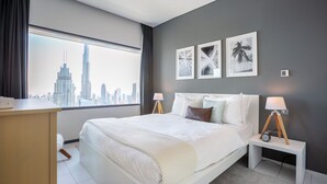 A modern hotel room with a large bed, two bedside tables with lamps, a city view, and three framed pictures on the wall. - Blueground | DIFC, pool, nr Dubai Fountain (Dubai)