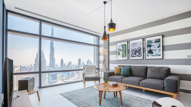 A modern living room with a large window, a grey sofa, a coffee table, and a lamp. - Blueground | DIFC, pool, nr Dubai Fountain (Dubai)