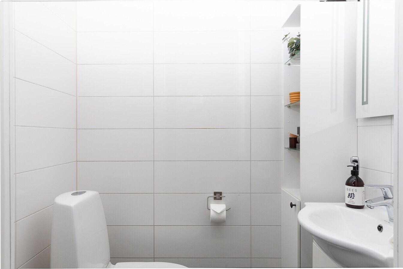 Une salle de bain moderne avec des carreaux blancs, des toilettes, un lavabo et un espace douche.