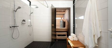 Une salle de bain moderne avec une douche, un banc en bois sur lequel sont posées des serviettes, et un sauna visible à travers une porte en verre.