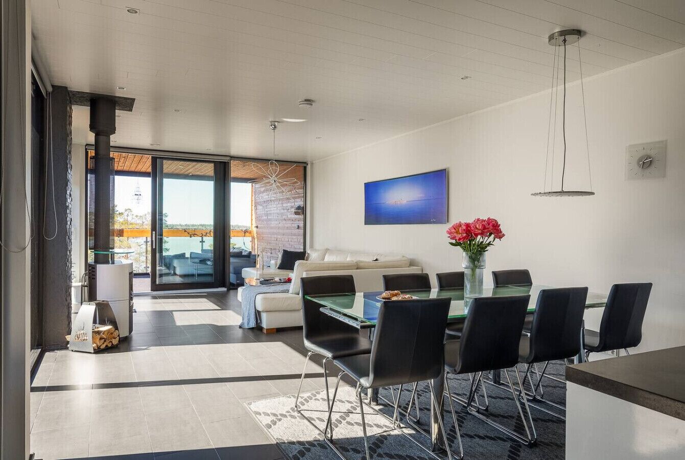 A modern living room with a glass dining table, black chairs, a sofa, and a TV.