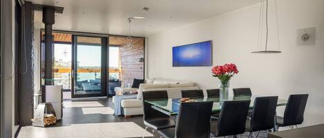 A modern living room with a glass dining table, black chairs, a sofa, and a TV.