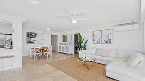 A spacious living area with a white sofa, a dining table with chairs, a coffee table, and a large plant. - Broadbeach Blvd Apartment (Broadbeach)