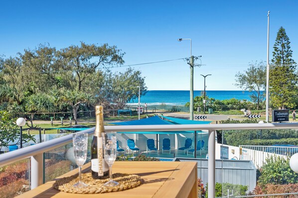 Une vue sur la piscine depuis le bord, avec une table sur laquelle se trouvent une bouteille et un verre, donnant sur la piscine et l’océan.