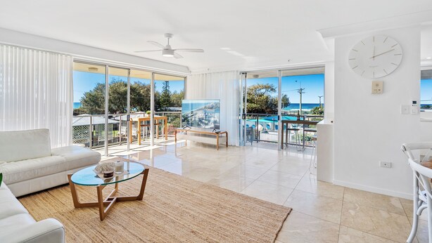 A spacious living area with a white sofa, a glass coffee table, and a view of the sea through large sliding glass doors. - Broadbeach Blvd Apartment (Broadbeach)