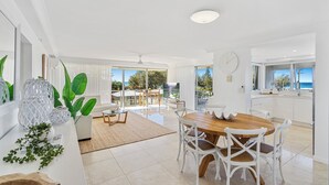 A bright, spacious kitchen with a wooden dining table and white chairs, large windows offering a view of the outdoors, and a modern, minimalist design. - Broadbeach Blvd Apartment (Broadbeach)