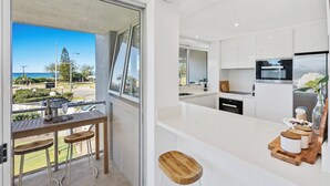 A modern kitchen with white cabinetry, a central island, and a view of the ocean. - Broadbeach Blvd Apartment (Broadbeach)