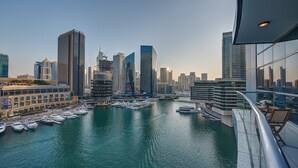 Une vue sur la ville, avec ses immeubles modernes et imposants, un port de plaisance rempli de bateaux, et une perspective depuis un balcon.