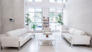 Een ruime woonkamer met twee witte banken, een salontafel en een boekenkast. Grote ramen zorgen voor daglicht en uitzicht op het omliggende landschap.