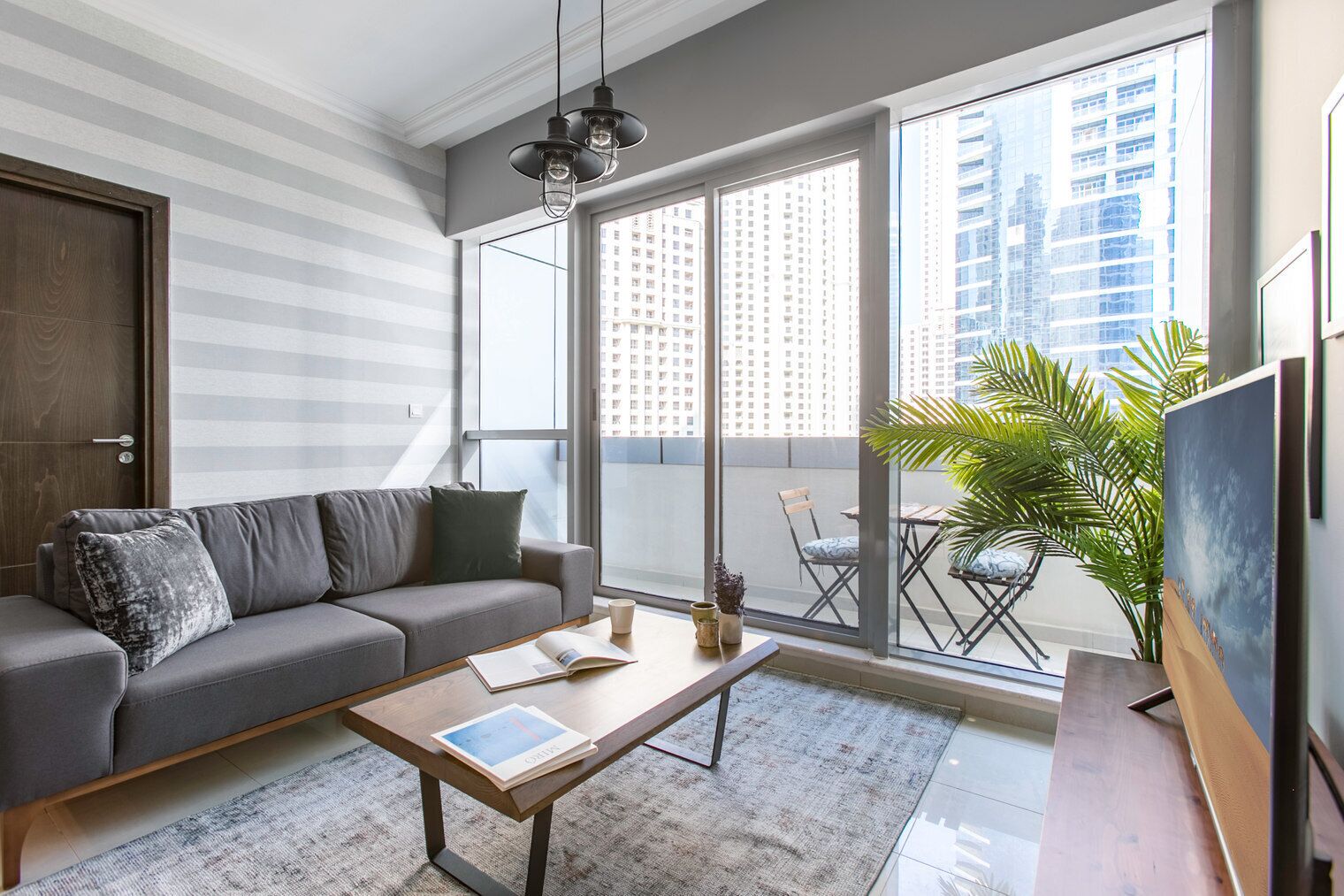 A modern living room with a grey sofa, a coffee table, and a large window overlooking a cityscape.
