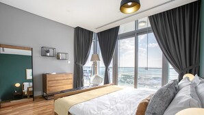 A modern bedroom with a large bed, a desk, a chair, a mirror, and a view of the city.