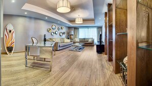 Un salon moderne avec un canapé, une table basse et un téléviseur. On peut voir une planche de surf accrochée au mur et le sol est recouvert de parquet.