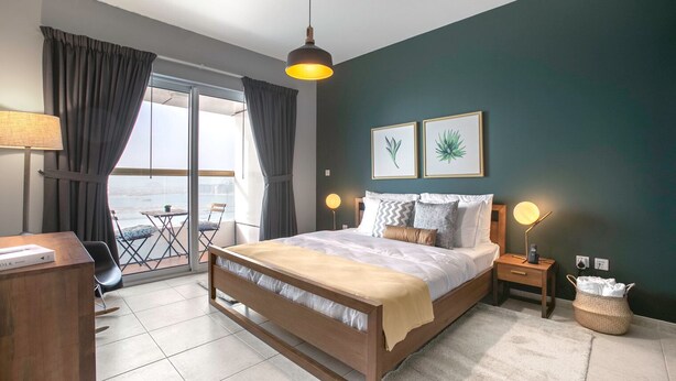 Une chambre à coucher avec un lit, des tables de chevet, une lampe, une vue sur l’extérieur et des œuvres d’art accrochées au mur.