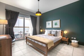 Ein Schlafzimmer mit Bett, Nachttischen, einer Lampe, Blick ins Freie und Kunstwerken an der Wand.