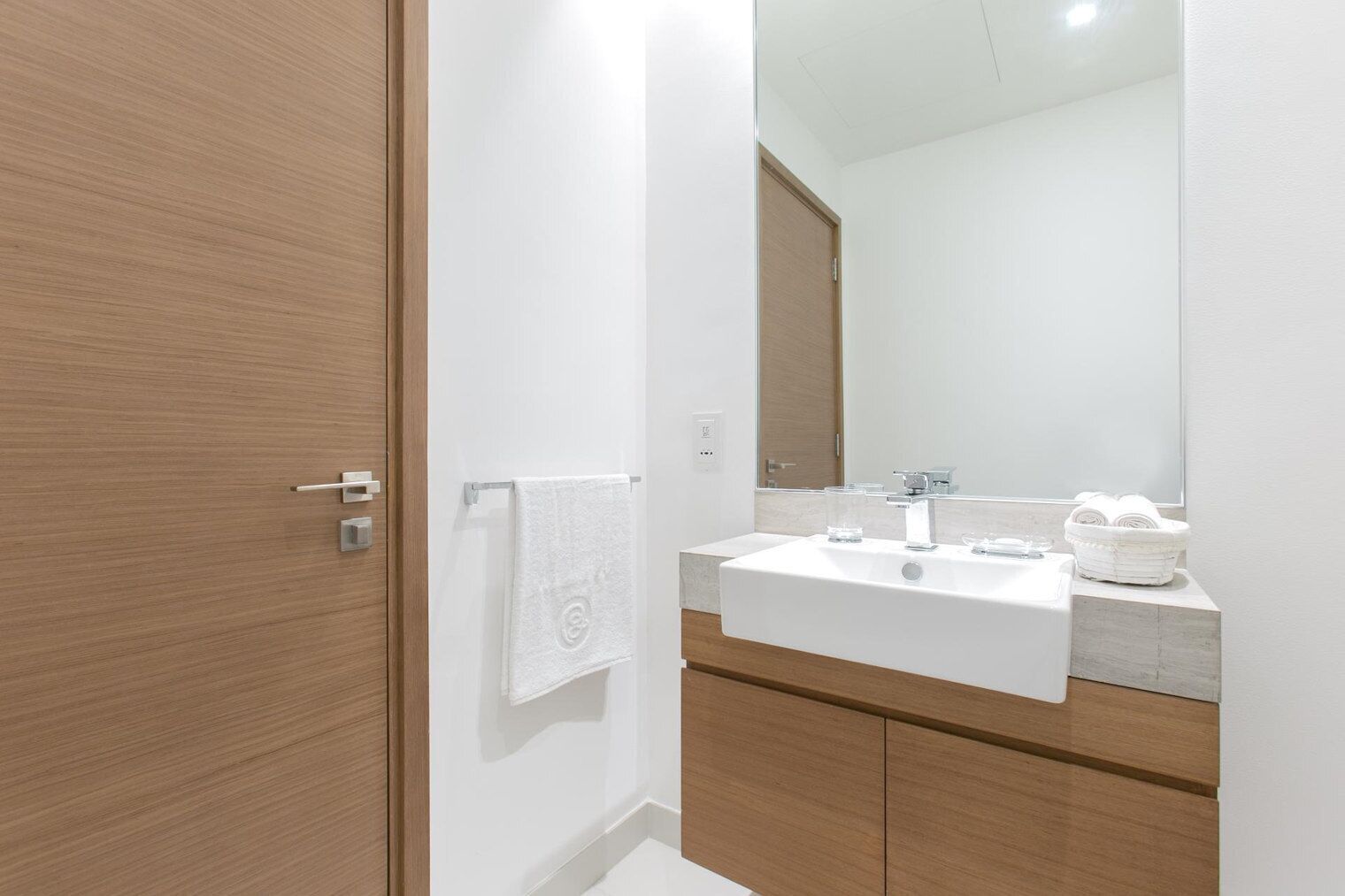 Une salle de bain moderne avec une porte en bois, un lavabo blanc et un miroir.
