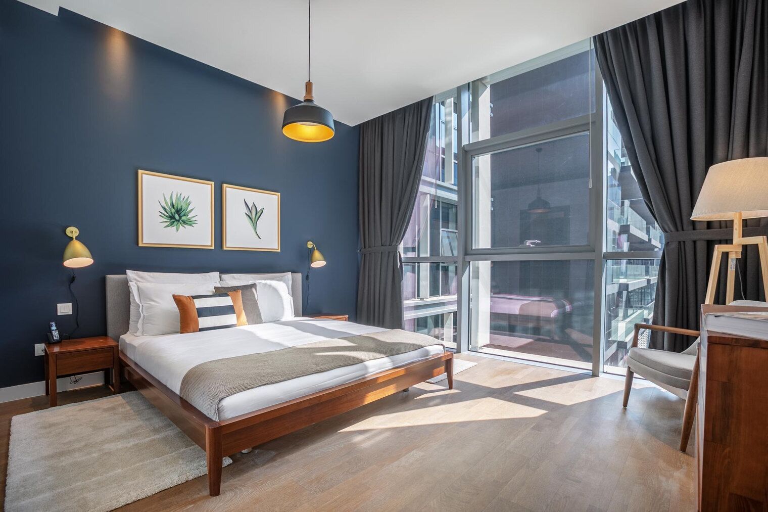 Camera da letto moderna con un letto grande, lampade sui comodini, vista sulla città attraverso ampie finestre e opere d'arte appese al muro.