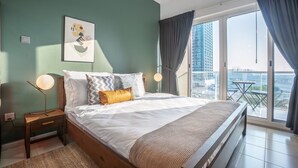 A modern bedroom with a large bed, a nightstand, a bedside lamp, and a view of the city through floor-to-ceiling windows. - Blueground | JLT, pool, nr Dubai Marina (Dubai)