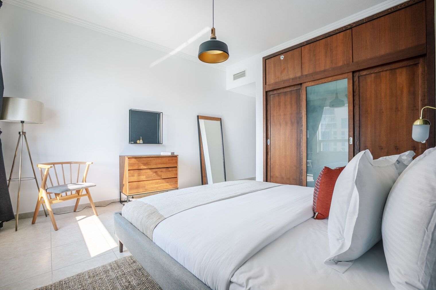 A modern bedroom with a large bed, wooden wardrobe, and a desk with a chair.