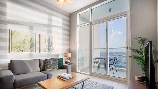 Un salon moderne avec un canapé gris, une table basse en bois et un balcon offrant une vue sur la ville.