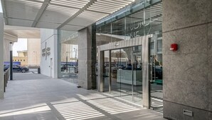 Une entrée moderne avec une porte en verre, un système d’alarme incendie et un espace de stationnement visible à travers le verre.