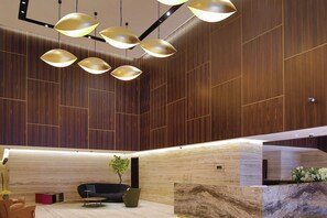 A modern interior with wooden paneling, a black sofa, a green chair, and a marble reception desk.