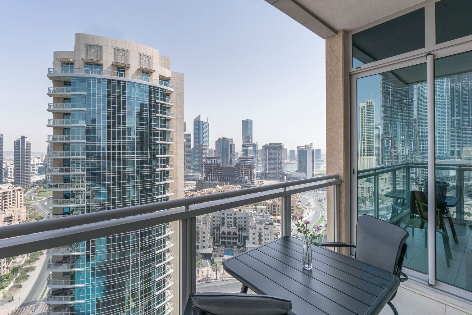 Un balcone con tavolo e sedie, che offre vista su un paesaggio urbano con edifici moderni.