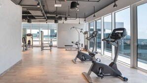 Una palestra moderna con macchinari cardio, attrezzature per l'allenamento con i pesi e ampie finestre che offrono vista sulla città.