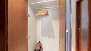 Un dressing accessible sans porte, avec des portes en bois, une tringle pour suspendre les vêtements et un aspirateur.