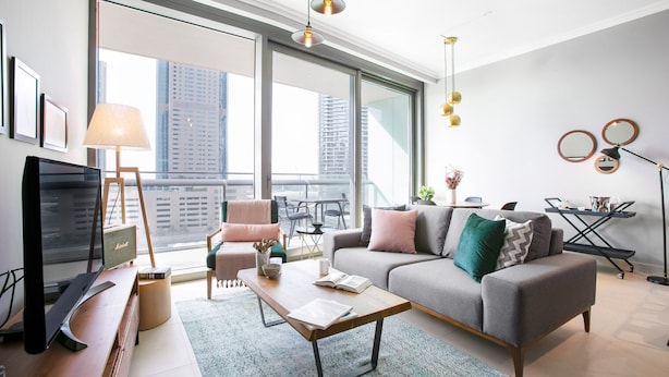 Un salon moderne avec un canapé gris, une table basse en bois et un téléviseur. Il y a un balcon avec vue sur les immebles.