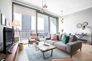 A modern living room with a grey sofa, a wooden coffee table, and a television. There is a balcony with a view of buildings. - Blueground | Downtown Dubai, pool, nr Burj Khalifa (Dubai)