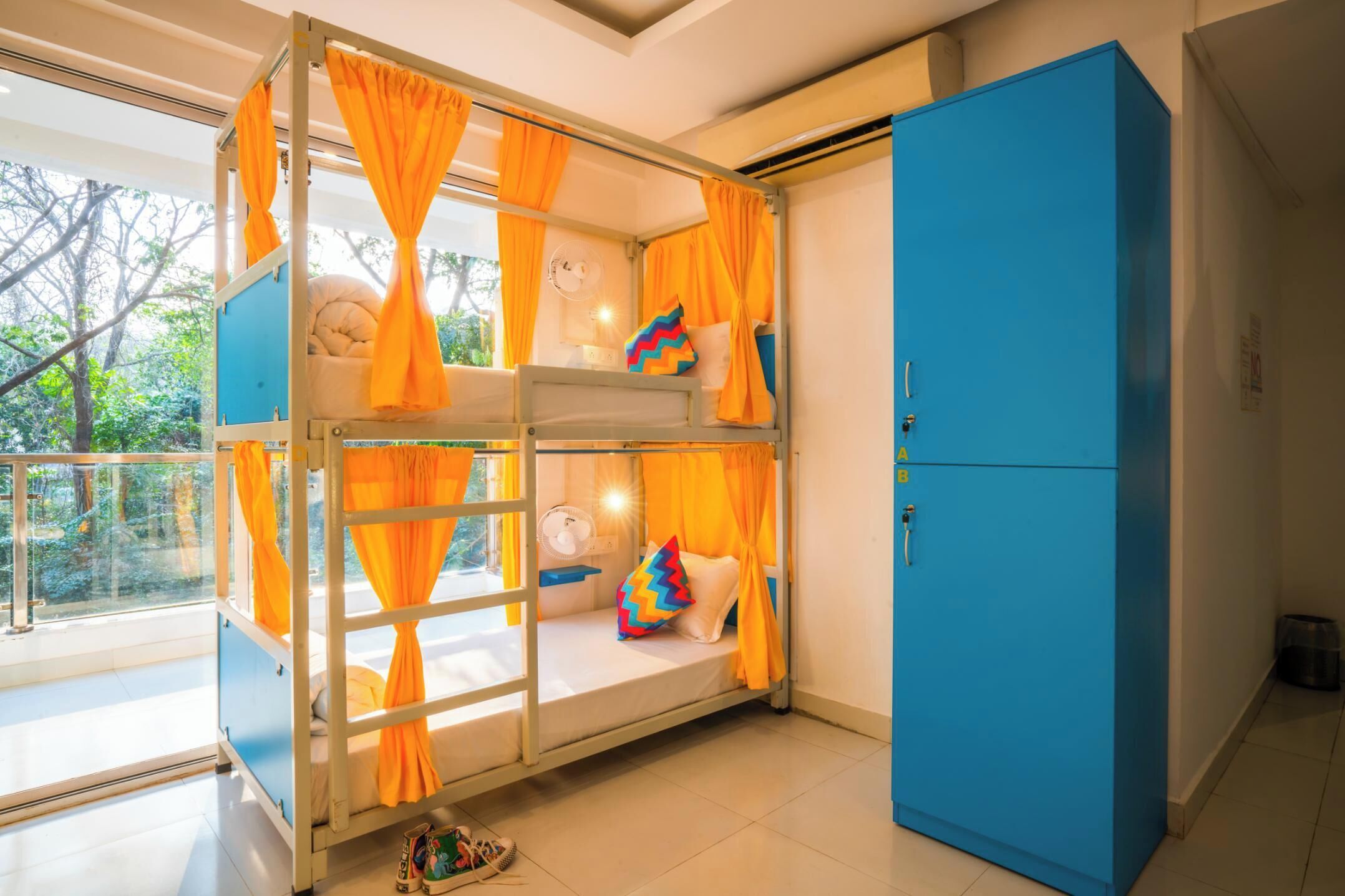 Una cama litera con cortinas naranjas, un armario azul y una ventana con vistas a árboles.
