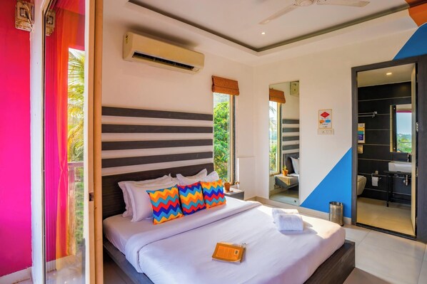 A hotel room with a bed, a window, an air conditioning unit, and a bathroom visible through an open door. - goSTOPS Goa Baga (Baga)