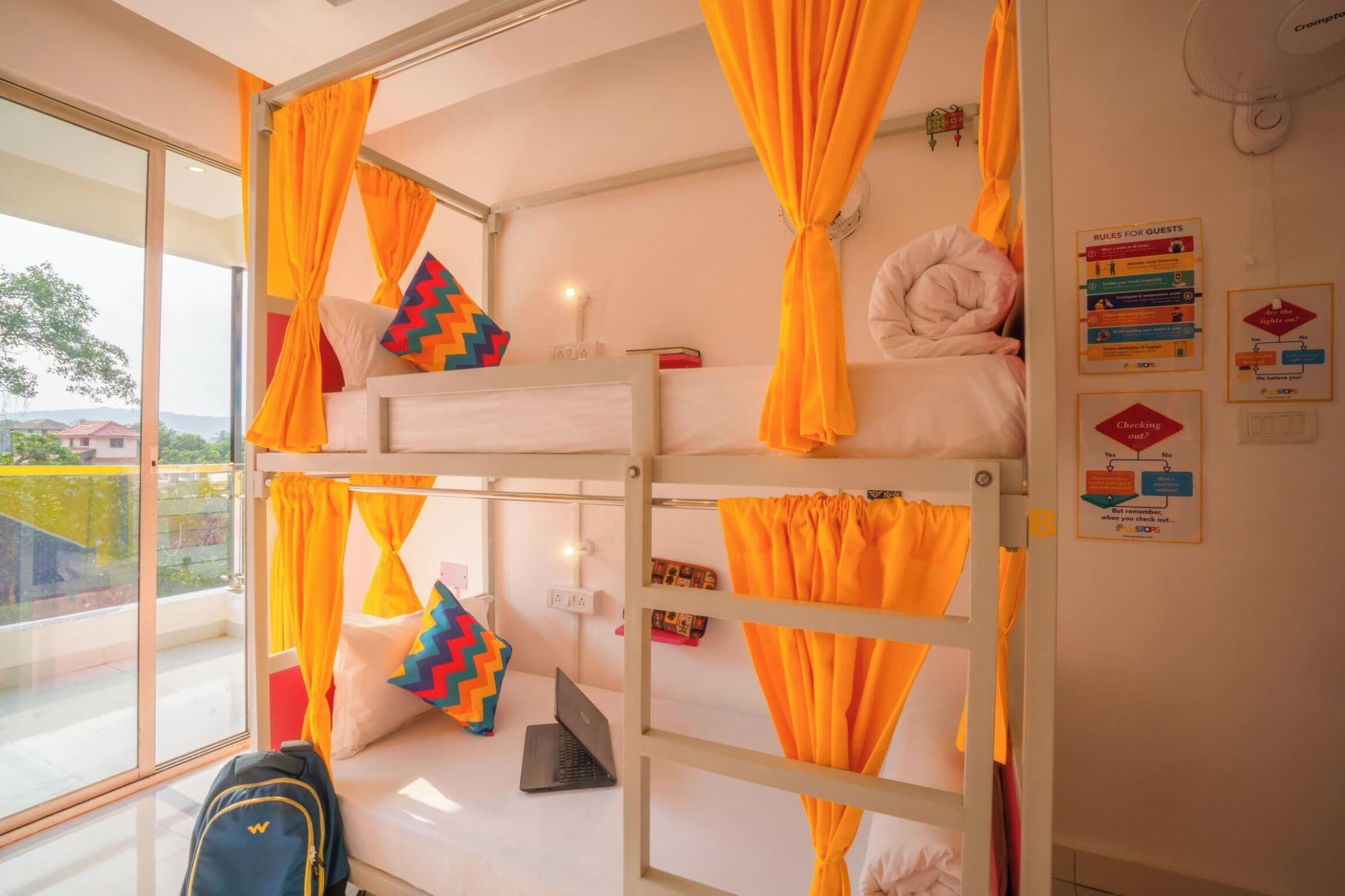 A bunk bed room with orange curtains, a laptop, and a pillow with a zigzag pattern.